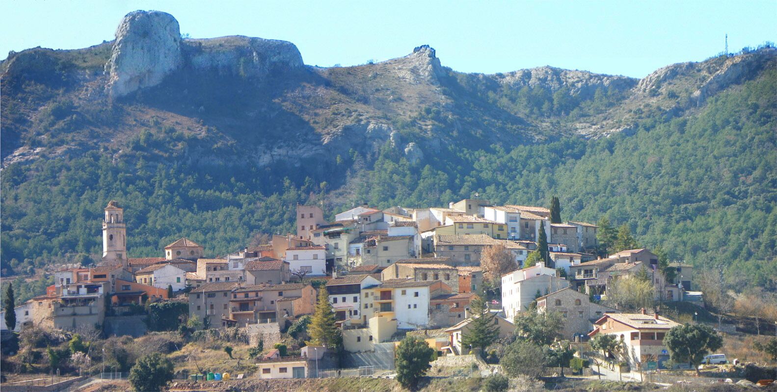 A hillside village with historic buildings, a prominent church tower, and a large rock formation in the background.