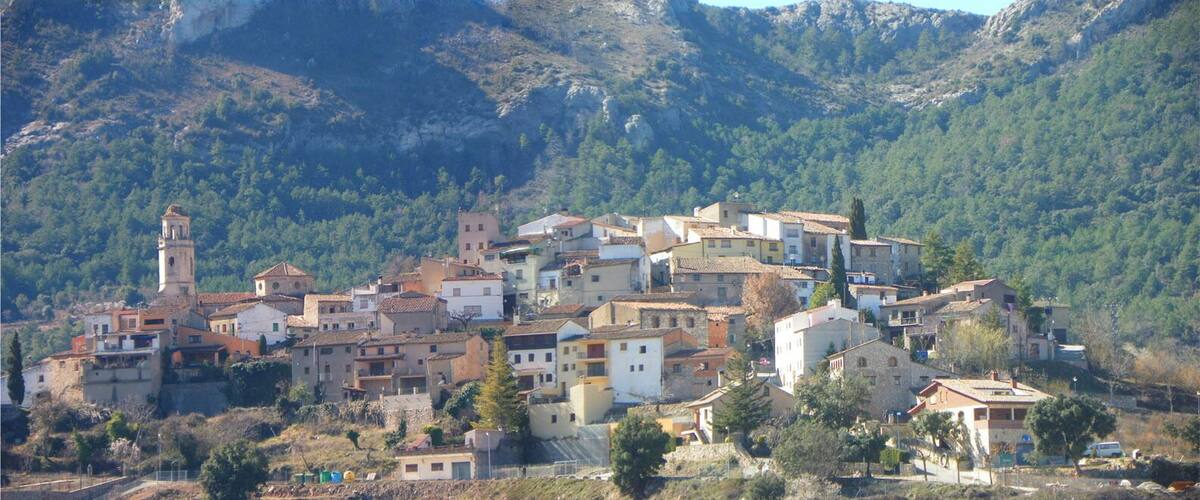 A hillside village with historic buildings, a prominent church tower, and a large rock formation in the background.