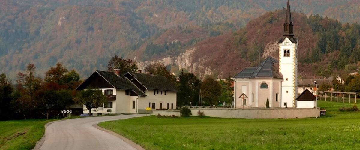 A church with a bell tower and a road curving through a valley with mountains in the background.