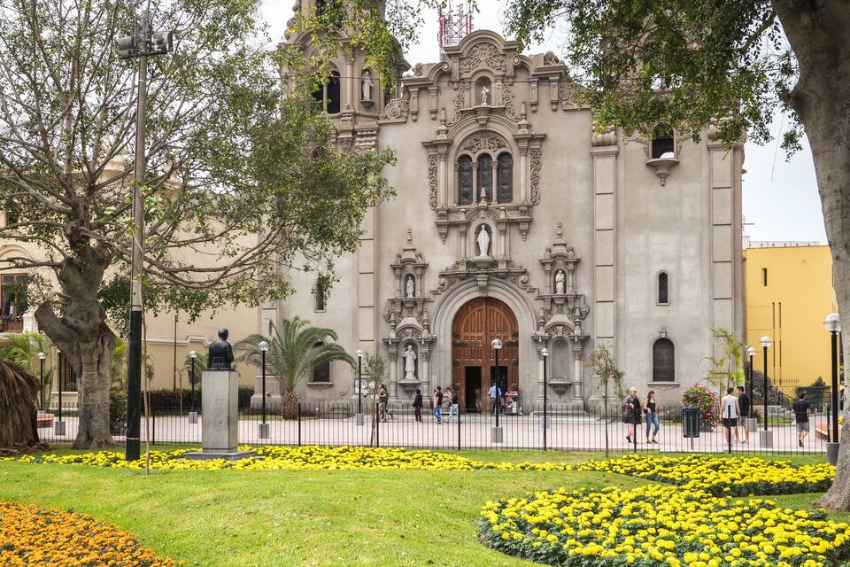 A historic building with ornate architecture, surrounded by a well-maintained garden with yellow flowers.