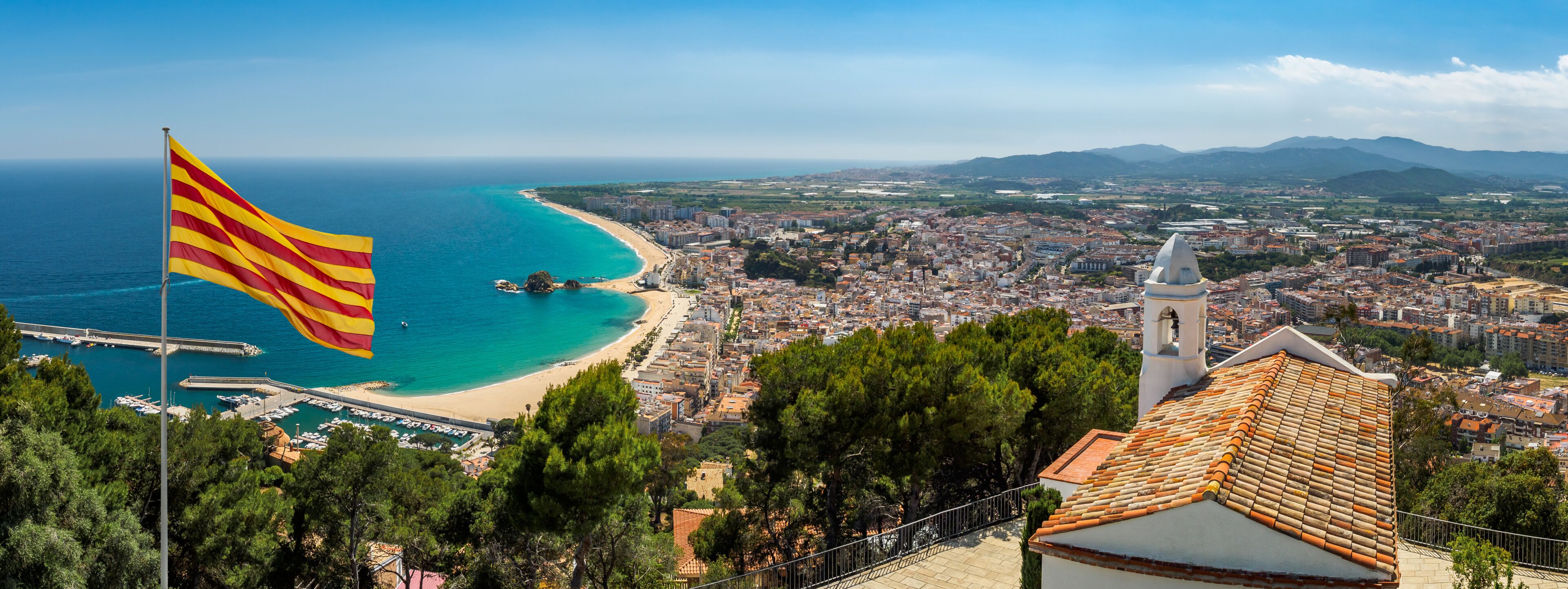 A coastal cityscape with a beach, a flag, and a church.