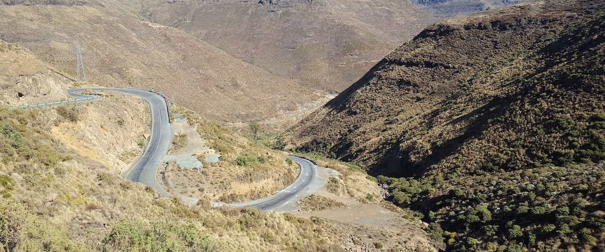 A winding mountain road surrounded by dry, rocky terrain and sparse vegetation.