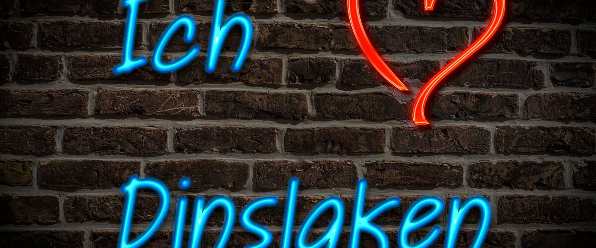 A neon sign with the text "Ich Dinslagen" and a heart symbol on a brick wall.