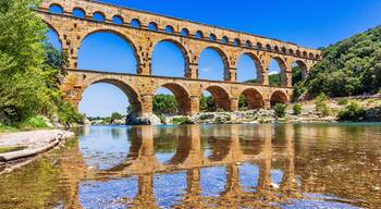 A stone aqueduct over a clear river with reflections, surrounded by greenery.