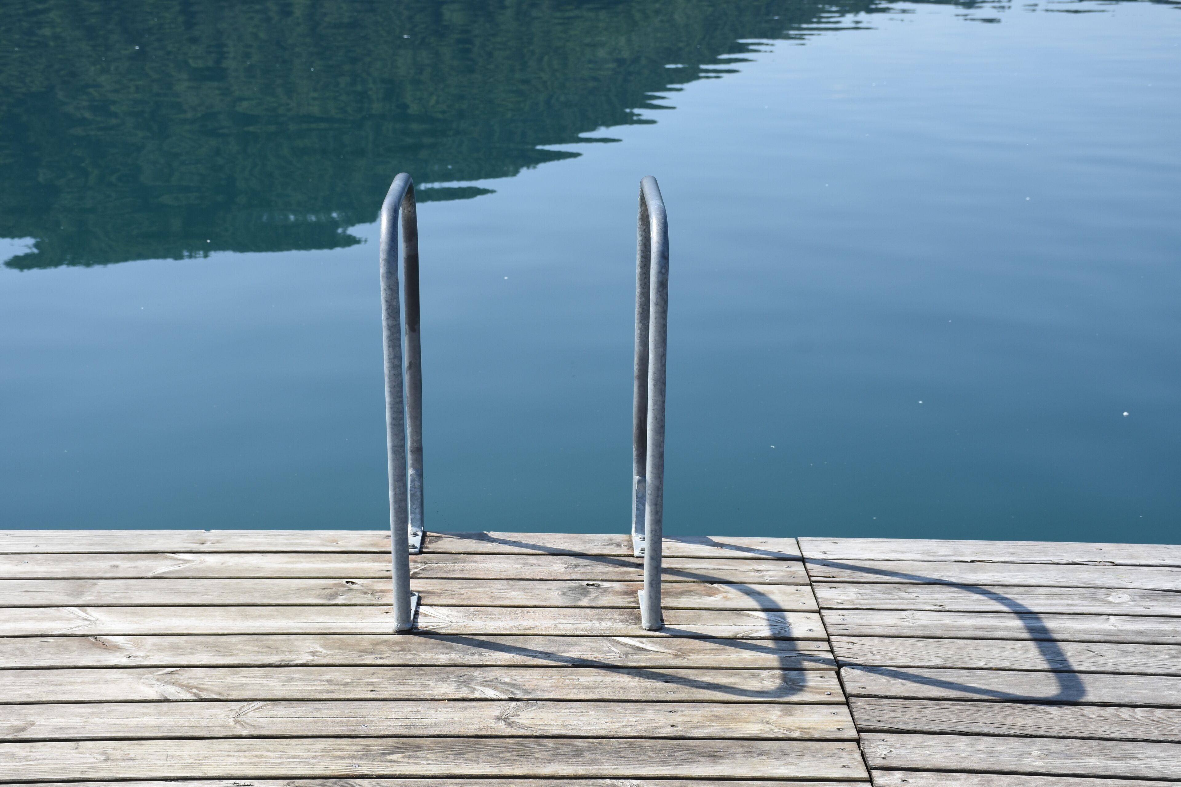 A wooden dock with metal railings extending into calm water.