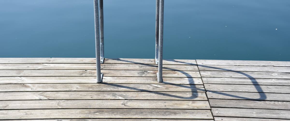 A wooden dock with metal railings extending into calm water.
