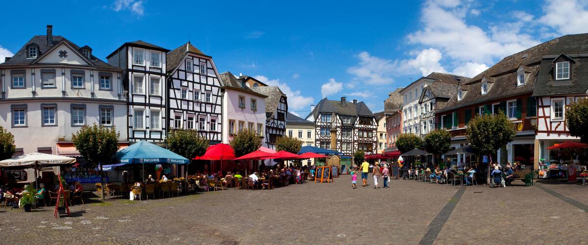 A cobblestone square with traditional half-timbered buildings, outdoor cafes, and pedestrians.