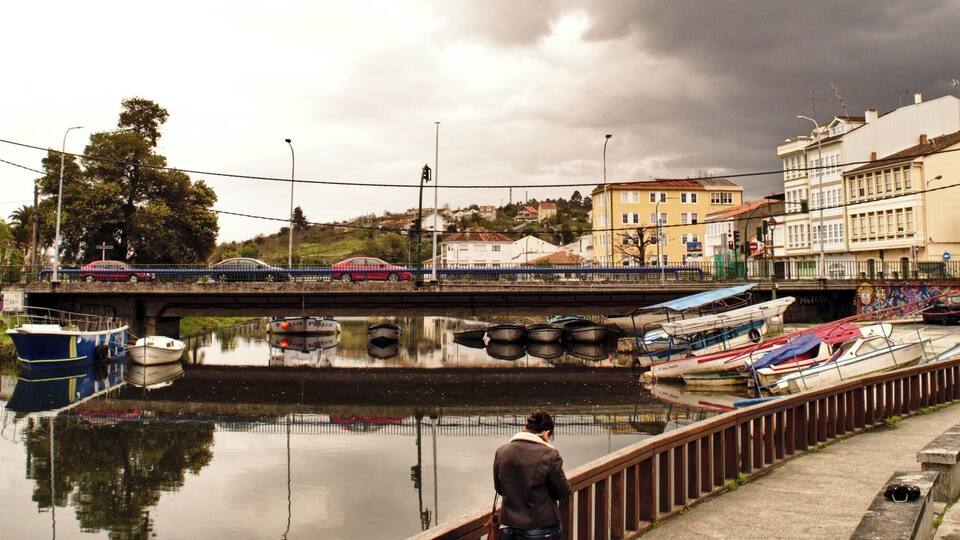 Un río con barcos amarrados, un puente y edificios al fondo.