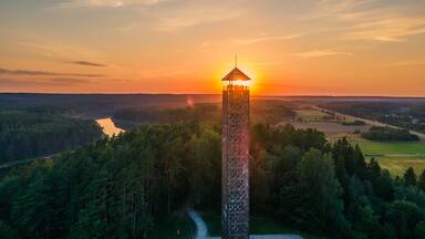 A tower with a viewing platform overlooking a forested valley at sunset.