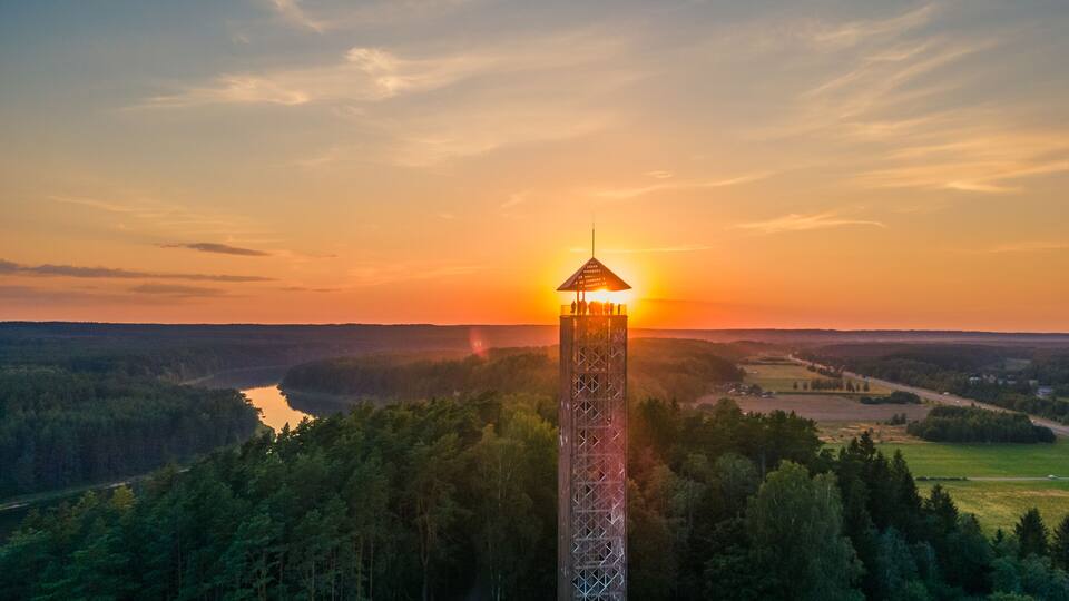A tower with a viewing platform overlooking a forested valley at sunset.