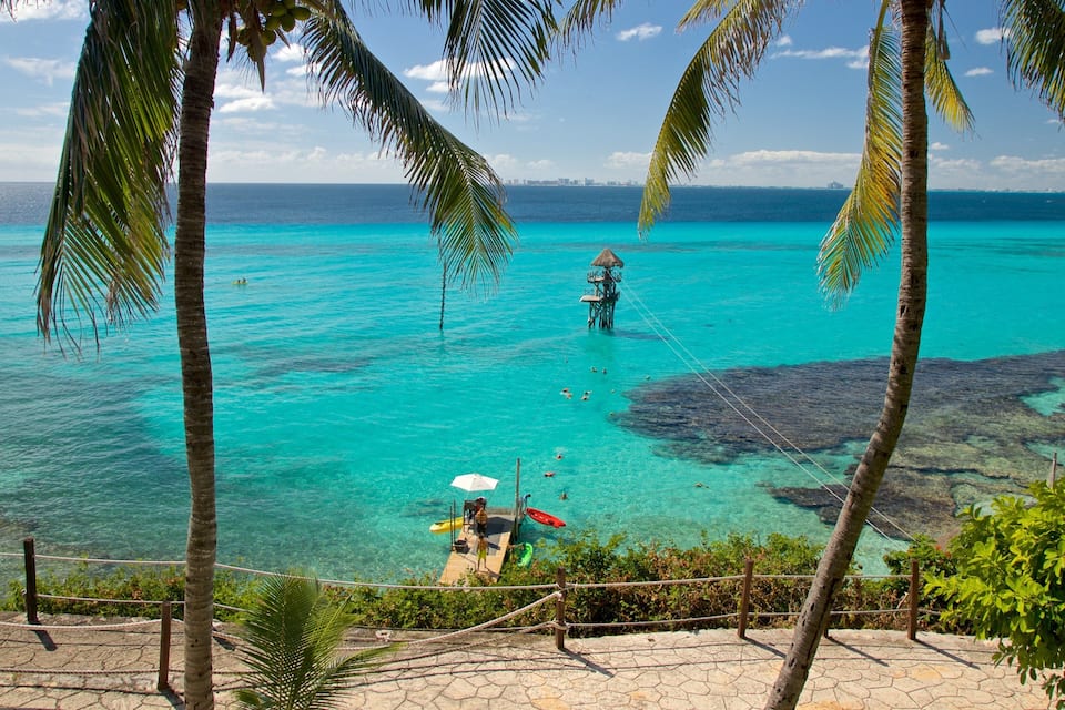 A turquoise sea with clear water, palm trees, and a person on a dock.