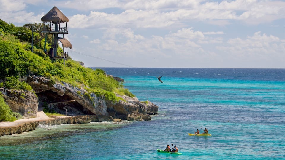 A coastal scene with a thatched-roof structure, clear turquoise waters, kayakers, and a person bungee jumping.