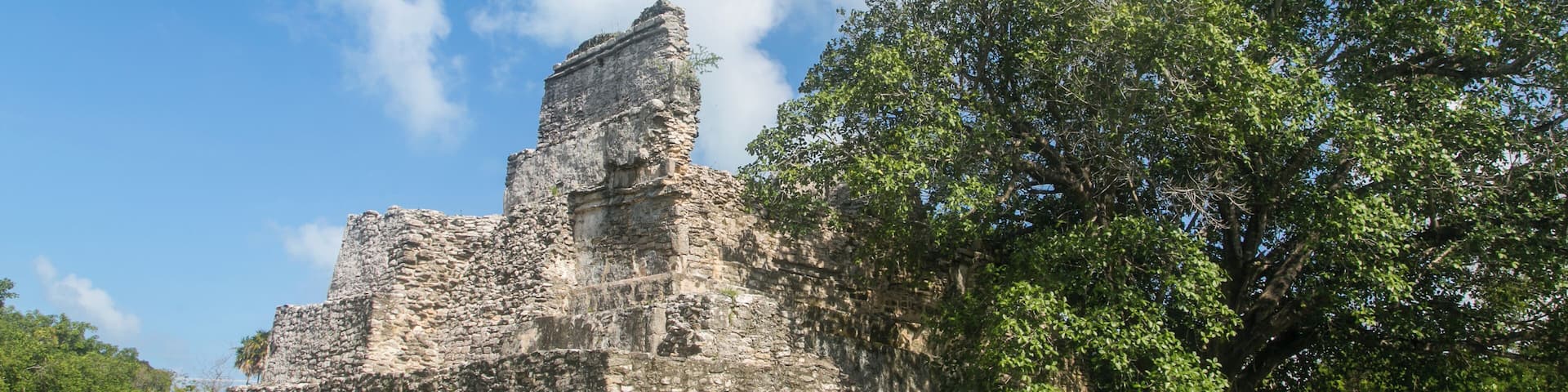 An ancient stone structure surrounded by lush green grass and trees under a clear blue sky.