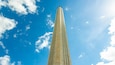 Un'alta e stretta torre sullo sfondo di un cielo azzurro con nuvole sparse.