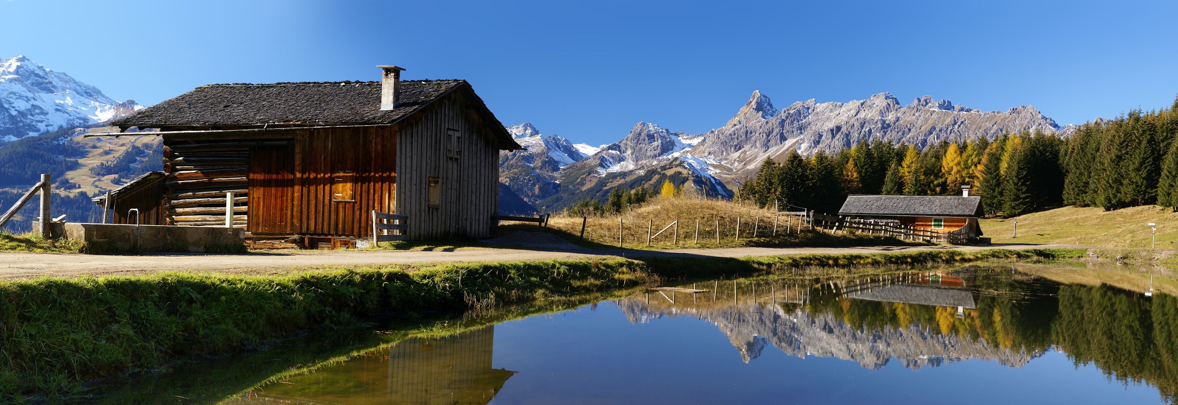 A wooden cabin by a calm lake with a mountain backdrop.