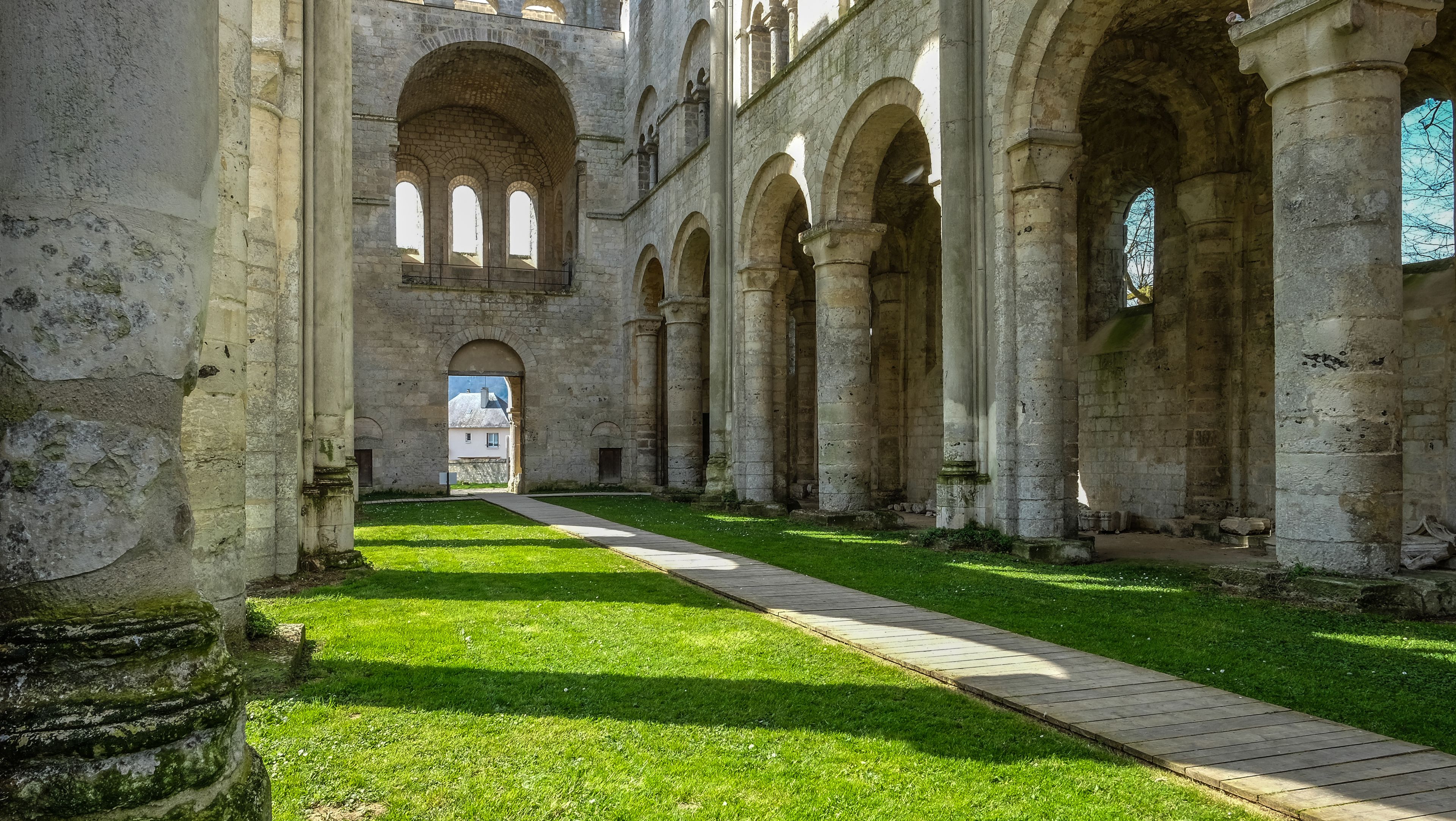 An ancient stone building with arched walkways and a grassy courtyard.