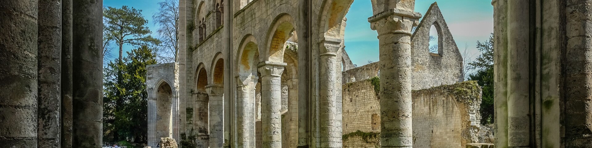 An ancient stone structure with multiple arches and columns, a paved pathway, and a grassy area.