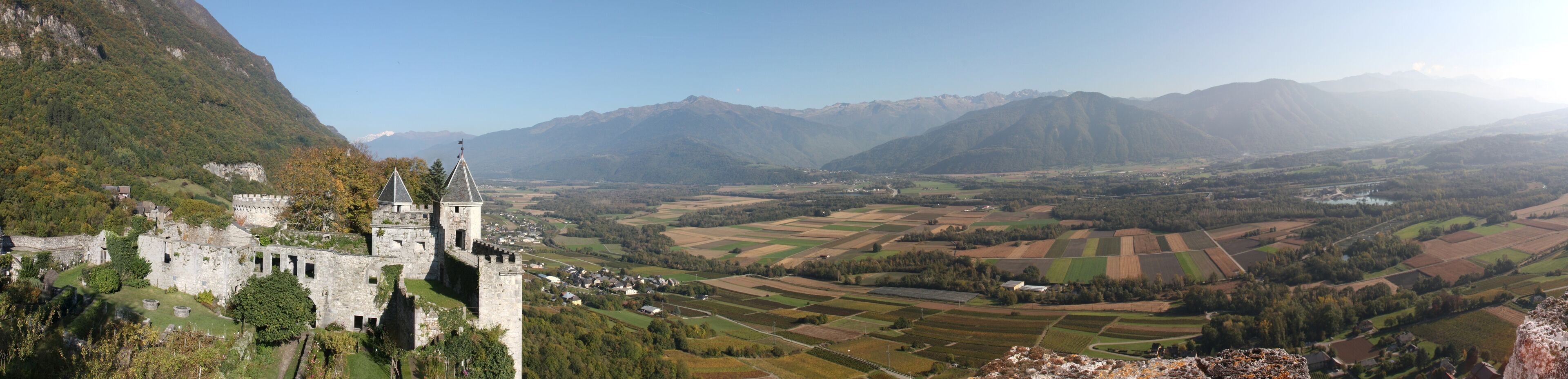 A castle on a hill overlooking a valley with fields and mountains in the background.