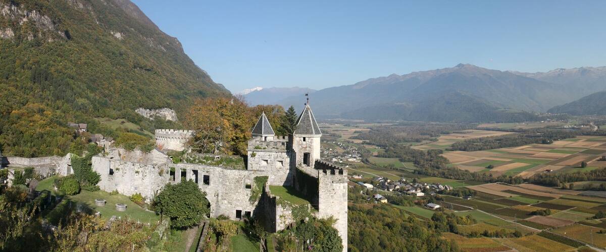 A castle on a hill overlooking a valley with fields and mountains in the background.