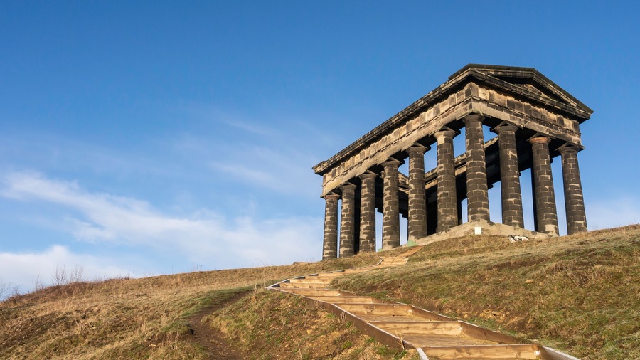 Un templo clásico con columnas sobre una colina cubierta de hierba bajo un cielo despejado.