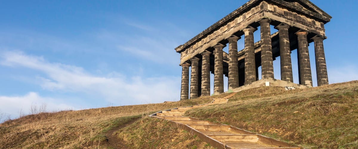 A classical temple with columns on a grassy hill under a clear sky.