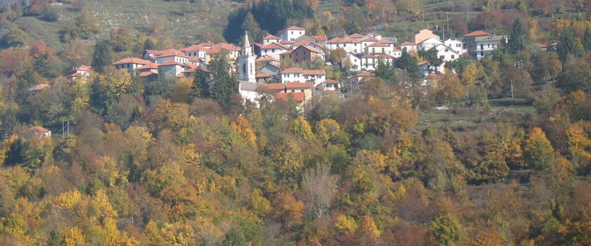 A village with red-roofed houses nestled in a valley surrounded by autumn-colored trees.