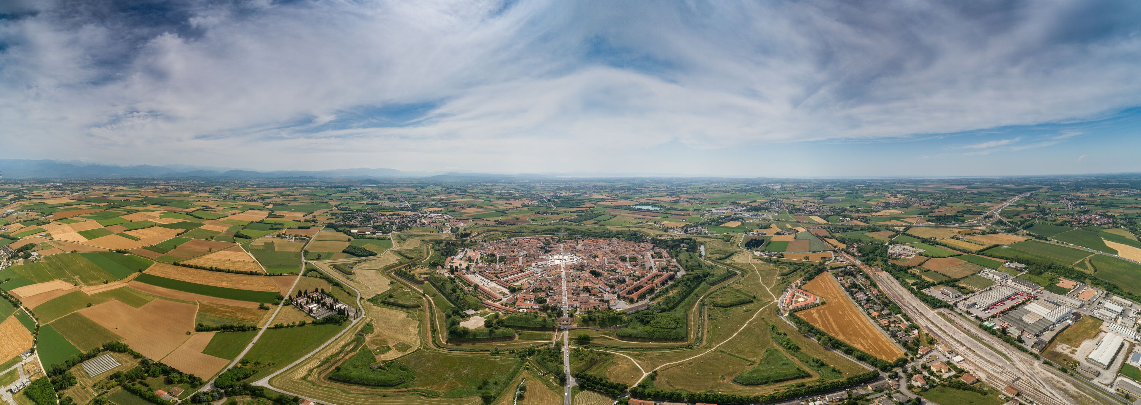 An aerial view of a town with a central square, surrounding fields, and distant mountains.