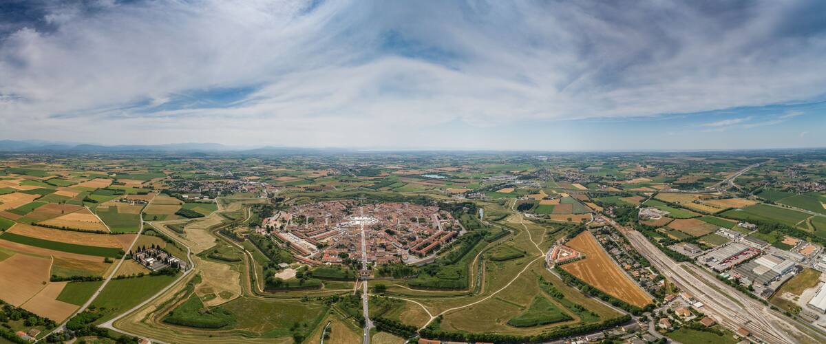 An aerial view of a town with a central square, surrounding fields, and distant mountains.