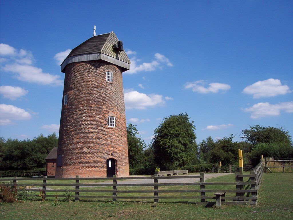A brick tower with a conical roof, surrounded by a wooden fence and greenery.