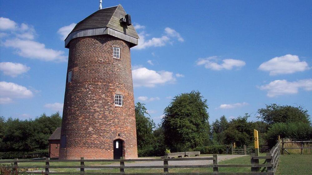 A brick tower with a conical roof, surrounded by a wooden fence and greenery.