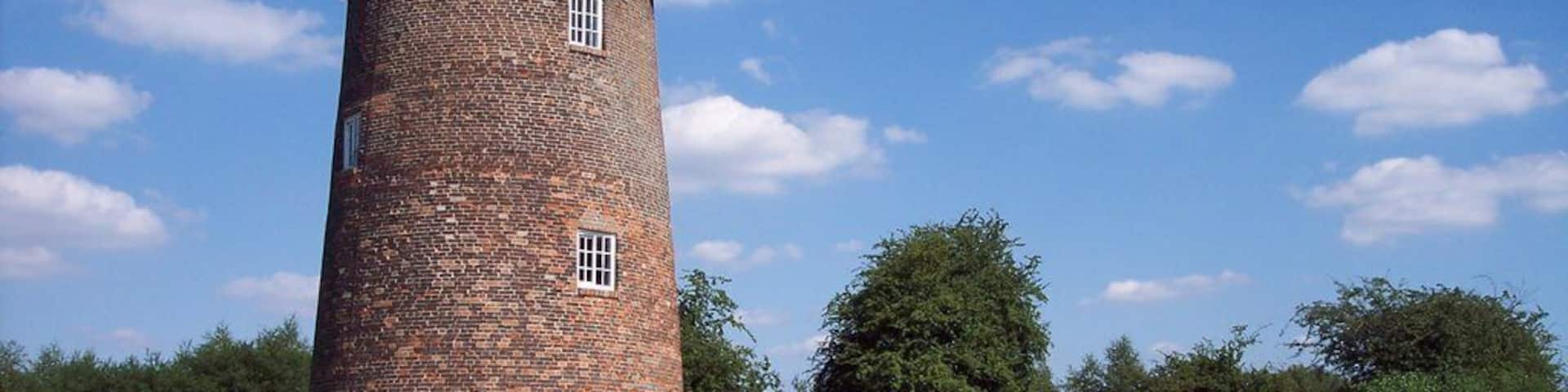 A brick tower with a conical roof, surrounded by a wooden fence and greenery.
