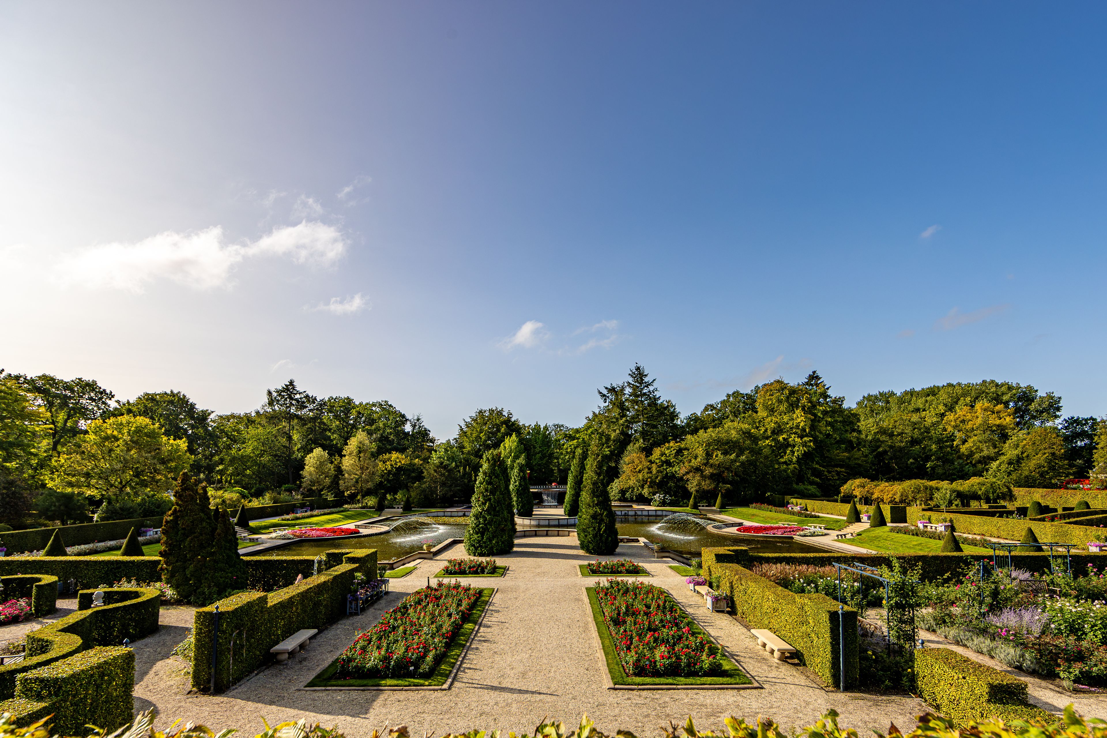 A formal garden with geometrically trimmed hedges, a central fountain, and a variety of flowering plants.