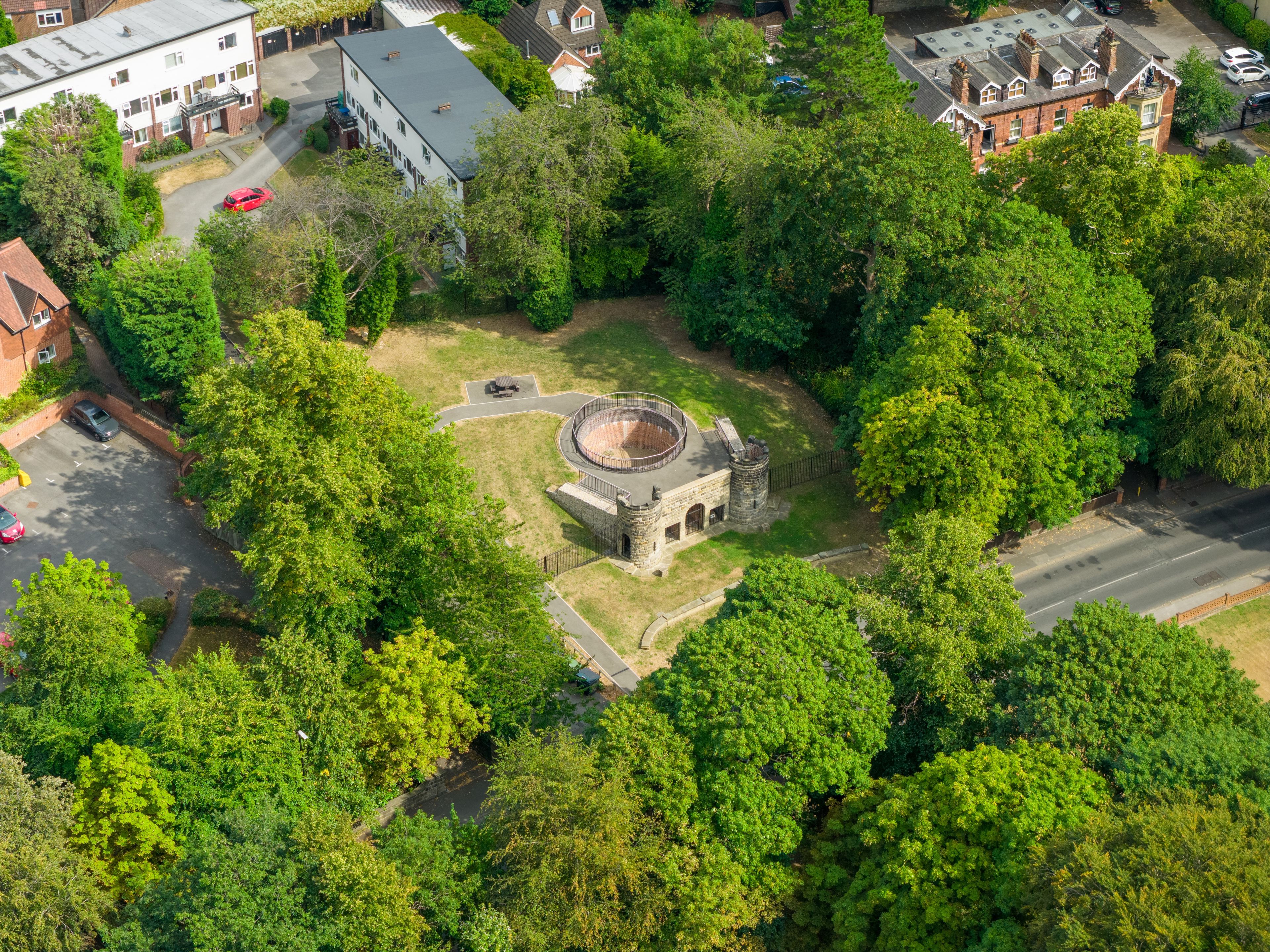 Vista aérea de un parque con una estructura de piedra circular rodeada de árboles frondosos.