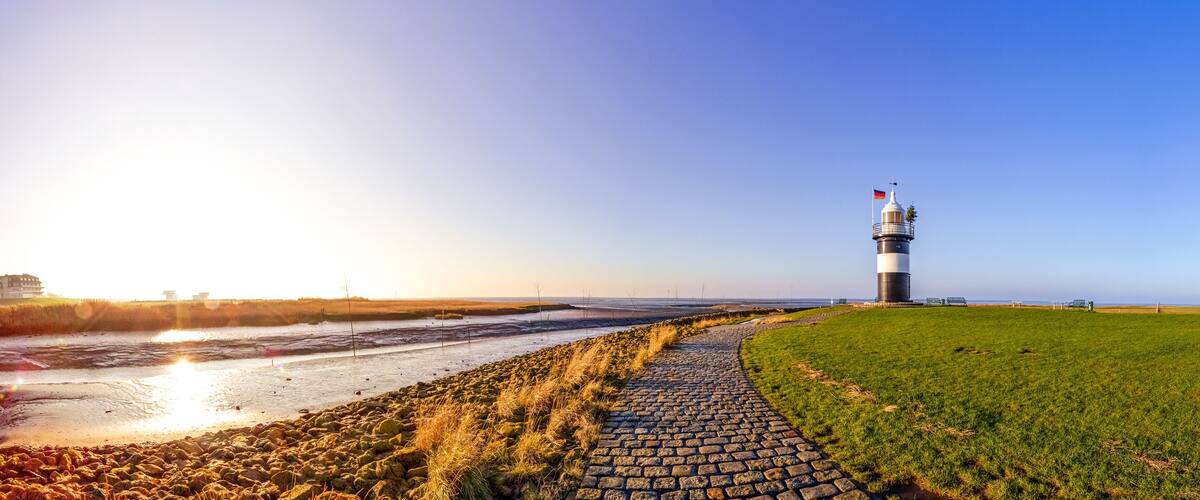 A lighthouse on a grassy hill with a cobblestone path leading to it.