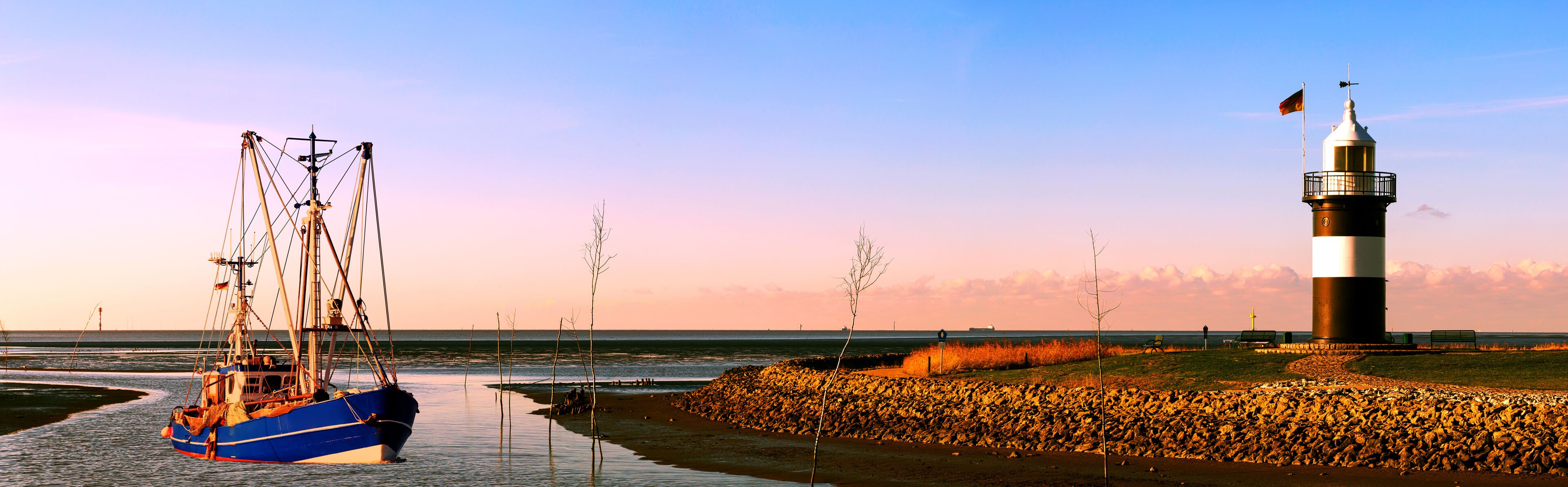 Krabbenkutter auf dem Heimweg bei Sonnenuntergang an der Nordseeküste, Kutterhafen in Wremen mit Leuchtturm 