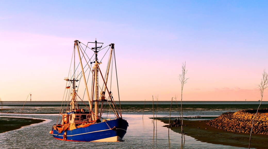 Krabbenkutter auf dem Heimweg bei Sonnenuntergang an der Nordseeküste, Kutterhafen in Wremen mit Leuchtturm