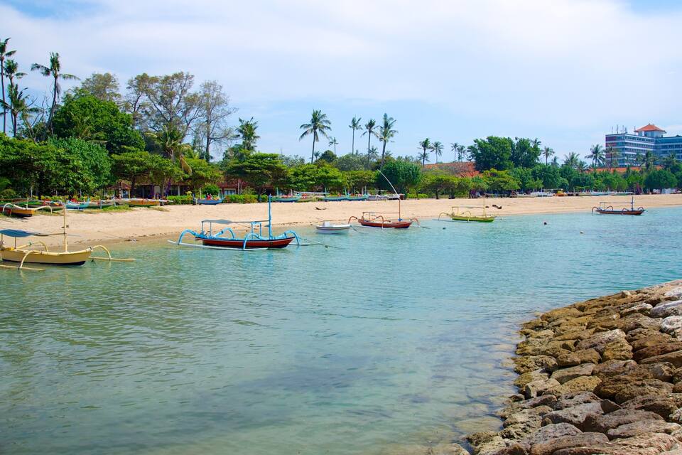 A beach with boats, palm trees, and a building in the background.
