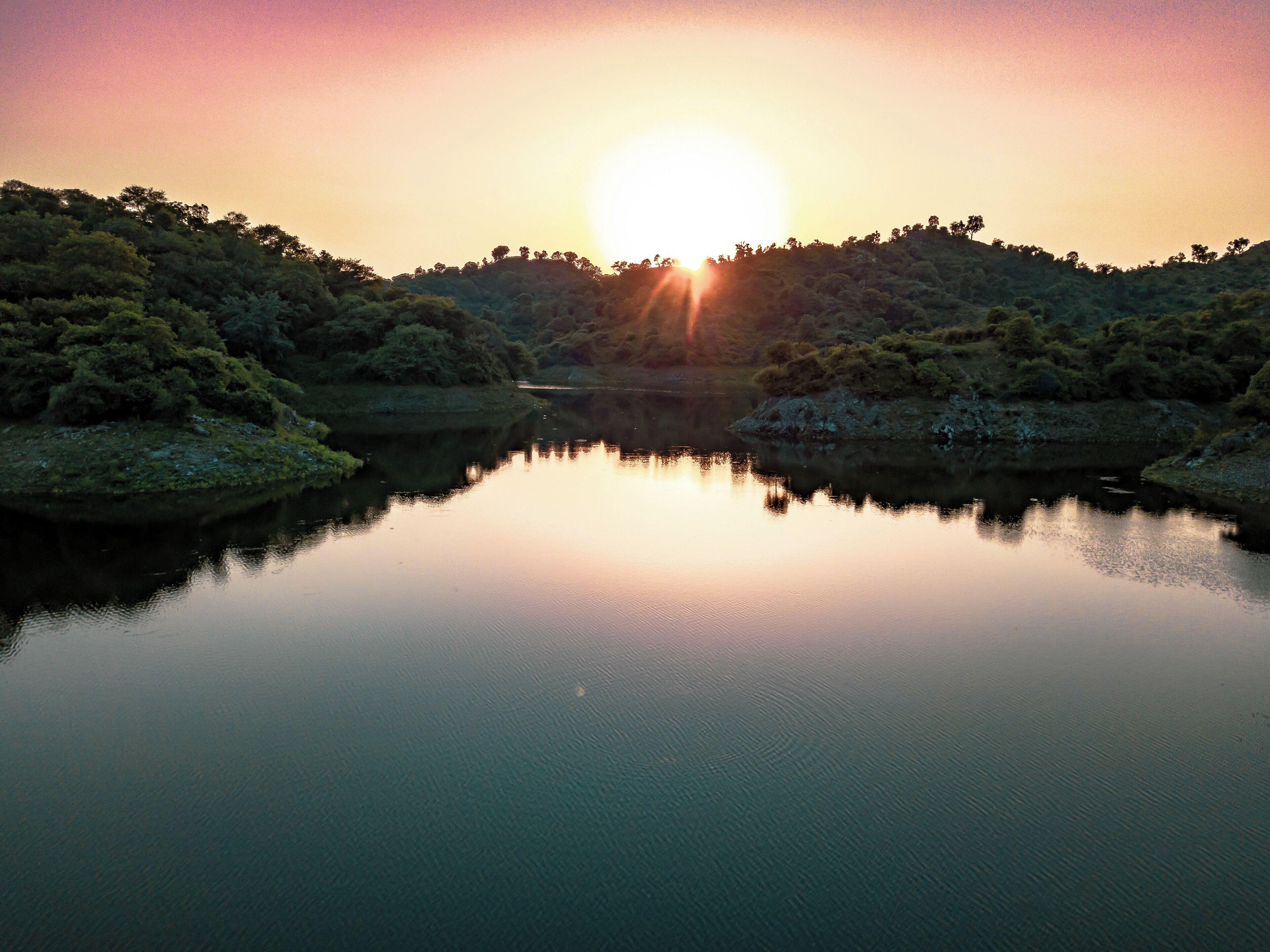 A calm lake at sunset with trees reflecting the sky.