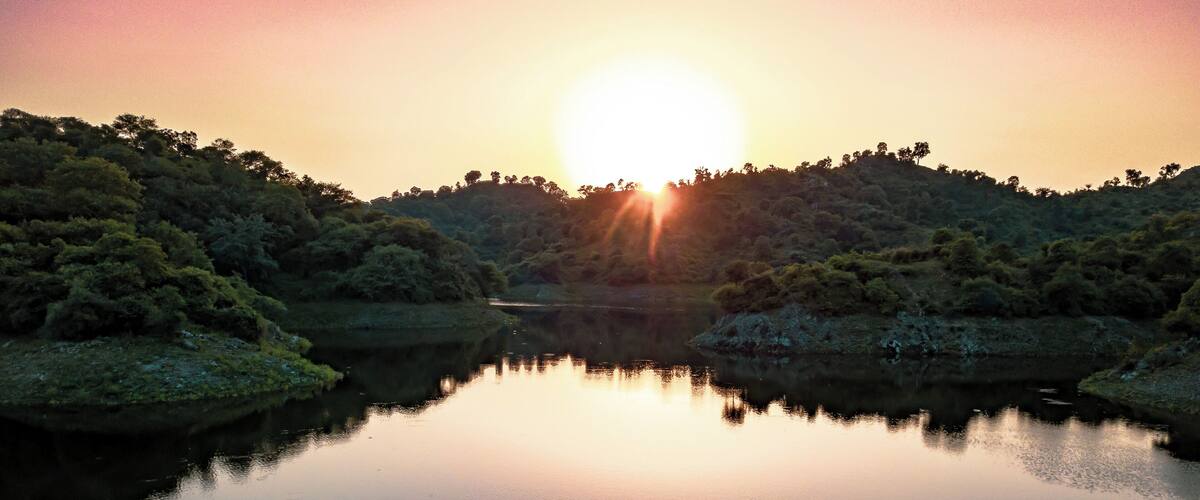 A calm lake at sunset with trees reflecting the sky.
