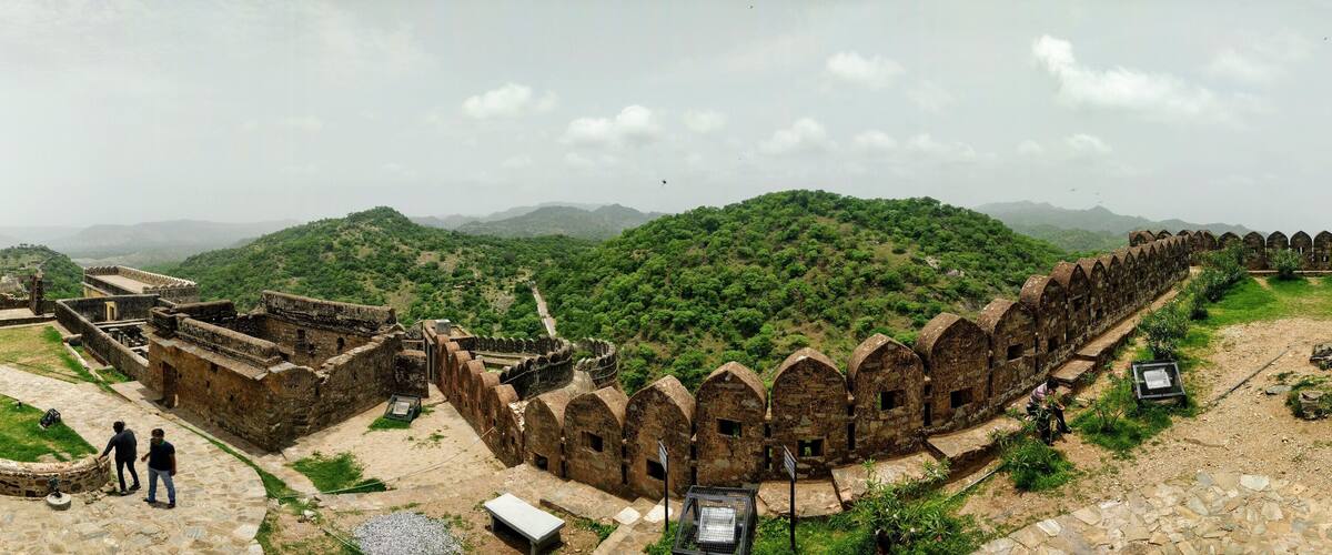 A historical fort with arched gateways and a lush green hill in the background.