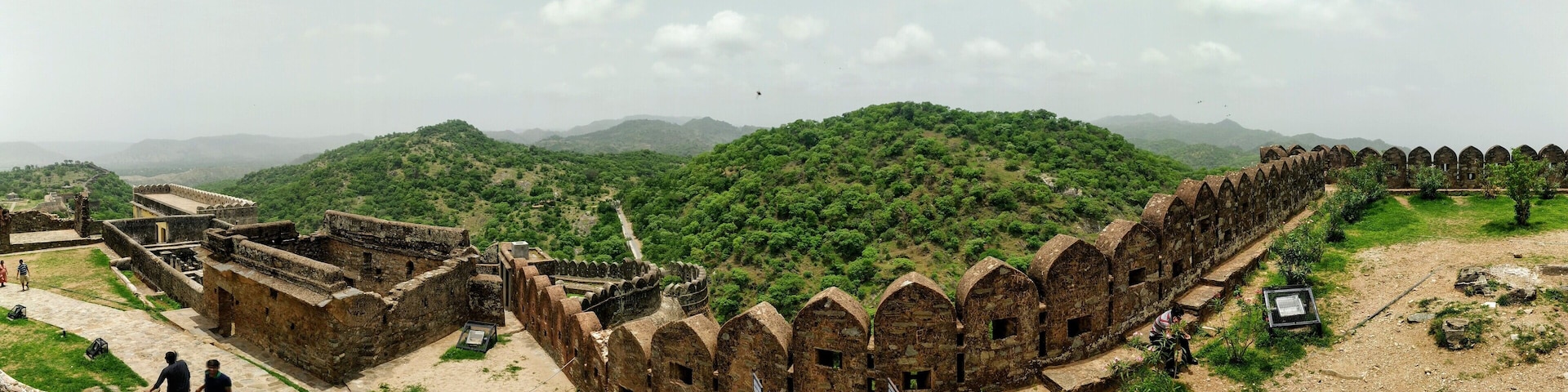 A historical fort with arched gateways and a lush green hill in the background.