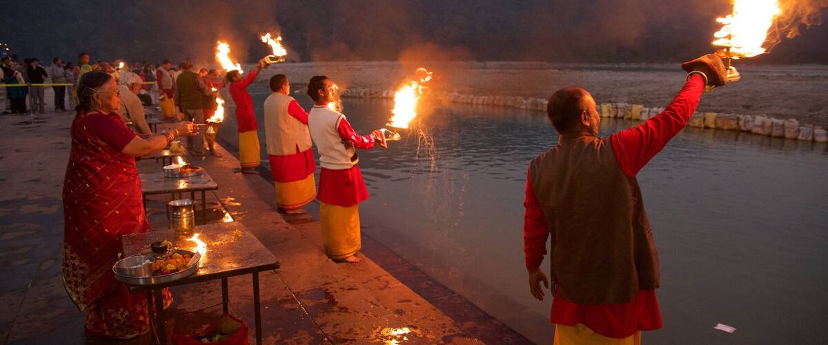 People holding torches on a lakeside at dusk.