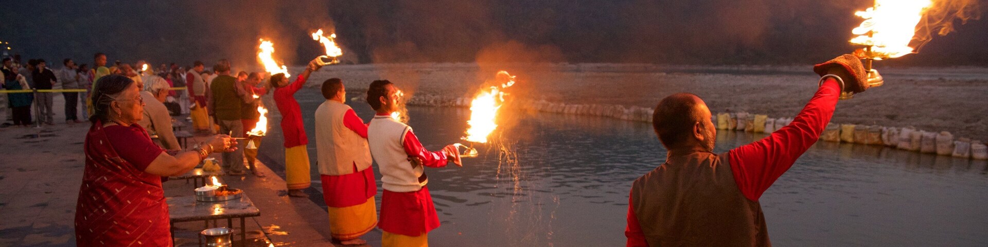 People holding torches on a lakeside at dusk.