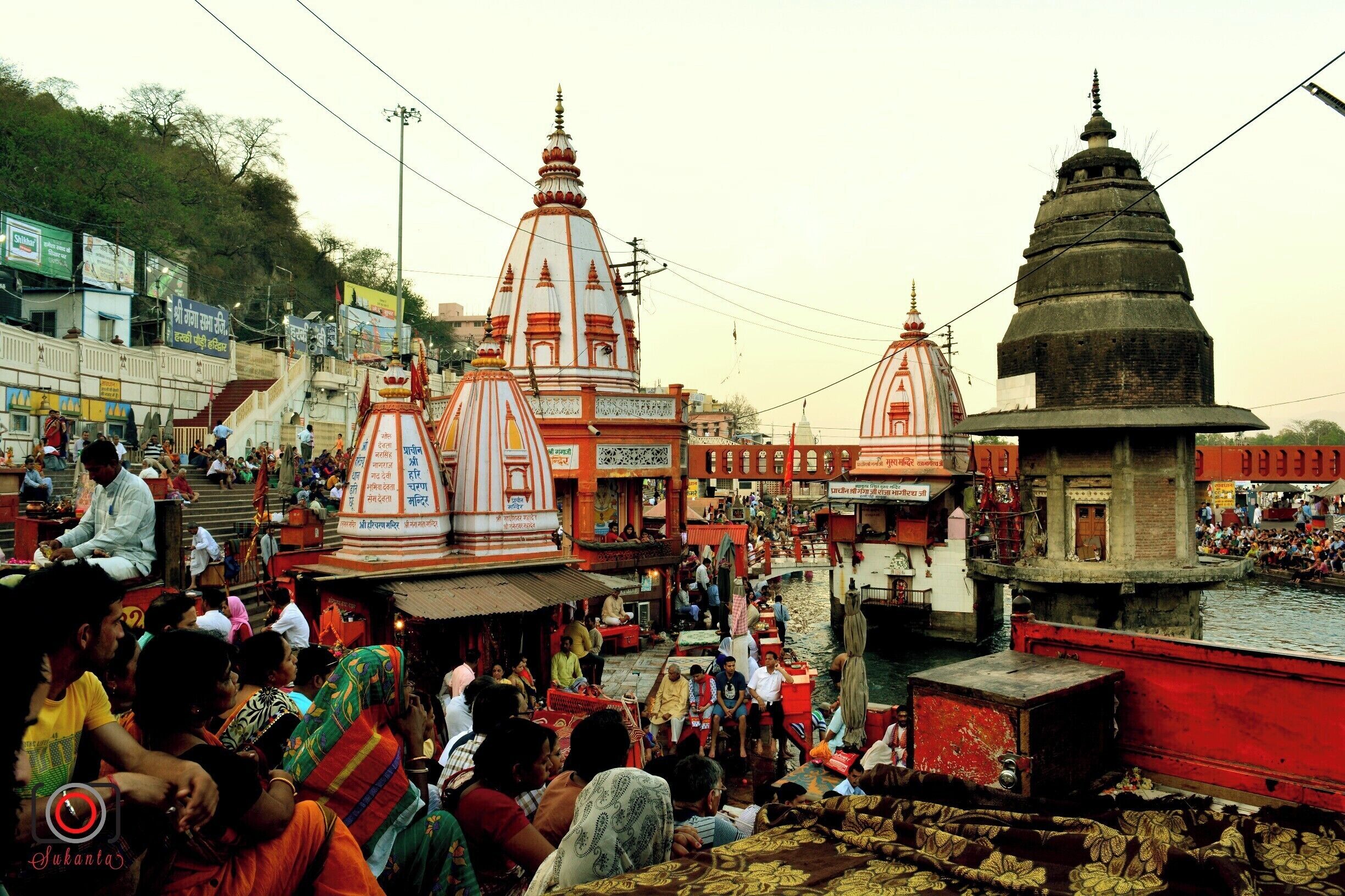 A crowded riverside area with temples and a large crowd of people.