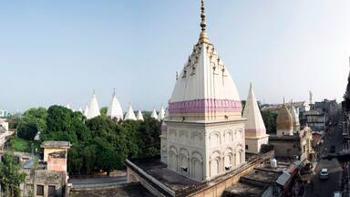 A white temple with a golden spire, surrounded by trees and urban buildings.