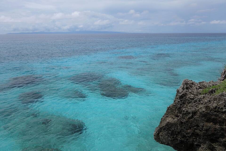 A coastal view with clear turquoise waters, rocky formations, and distant land.