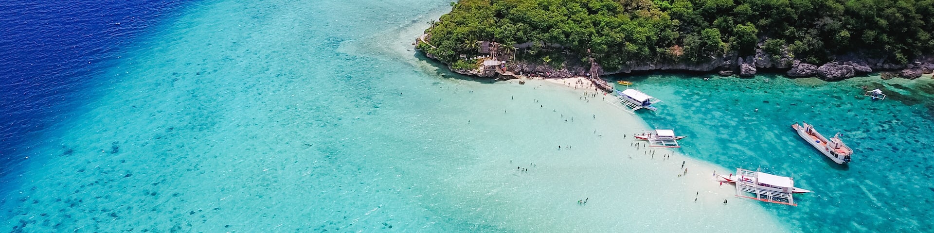 Aerial view of sandy beach with tourists swimming in beautiful clear sea water of the Sumilon island beach landing near Oslob, Cebu, Philippines. - Boost up color Processing. Panoramic banner.