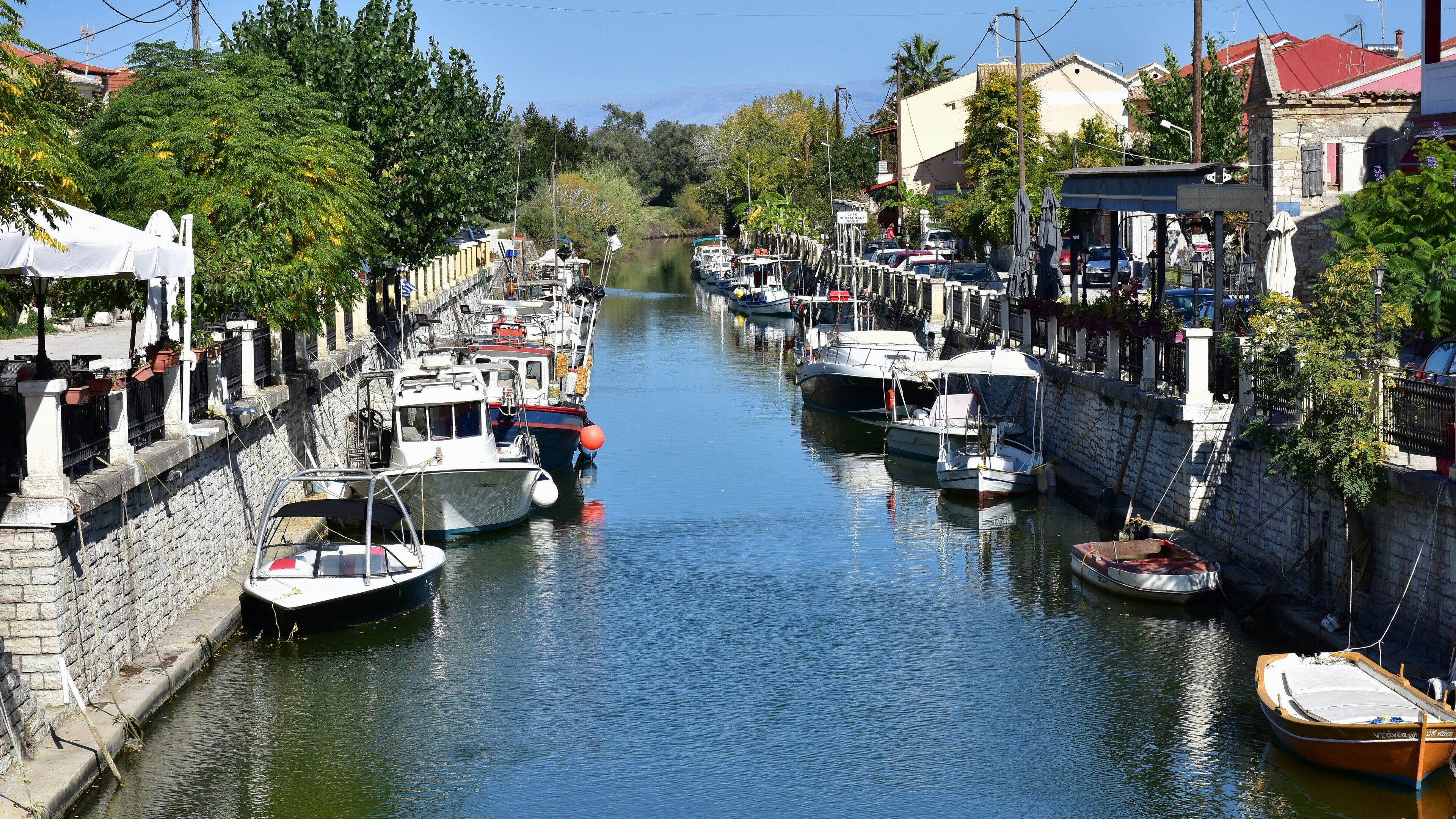 A narrow canal with boats docked along the sides, surrounded by stone walls and greenery.