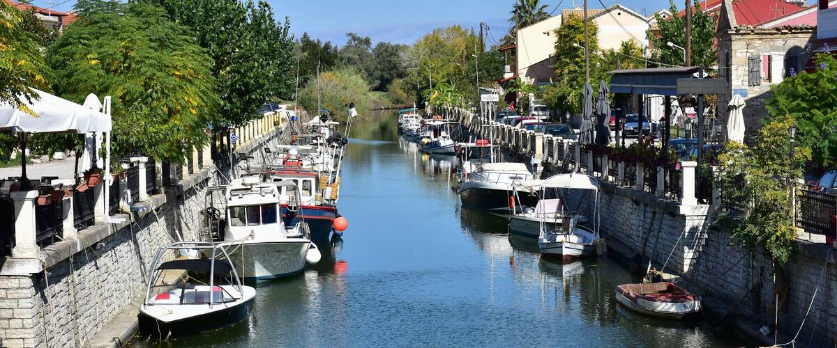 A narrow canal with boats docked along the sides, surrounded by stone walls and greenery.