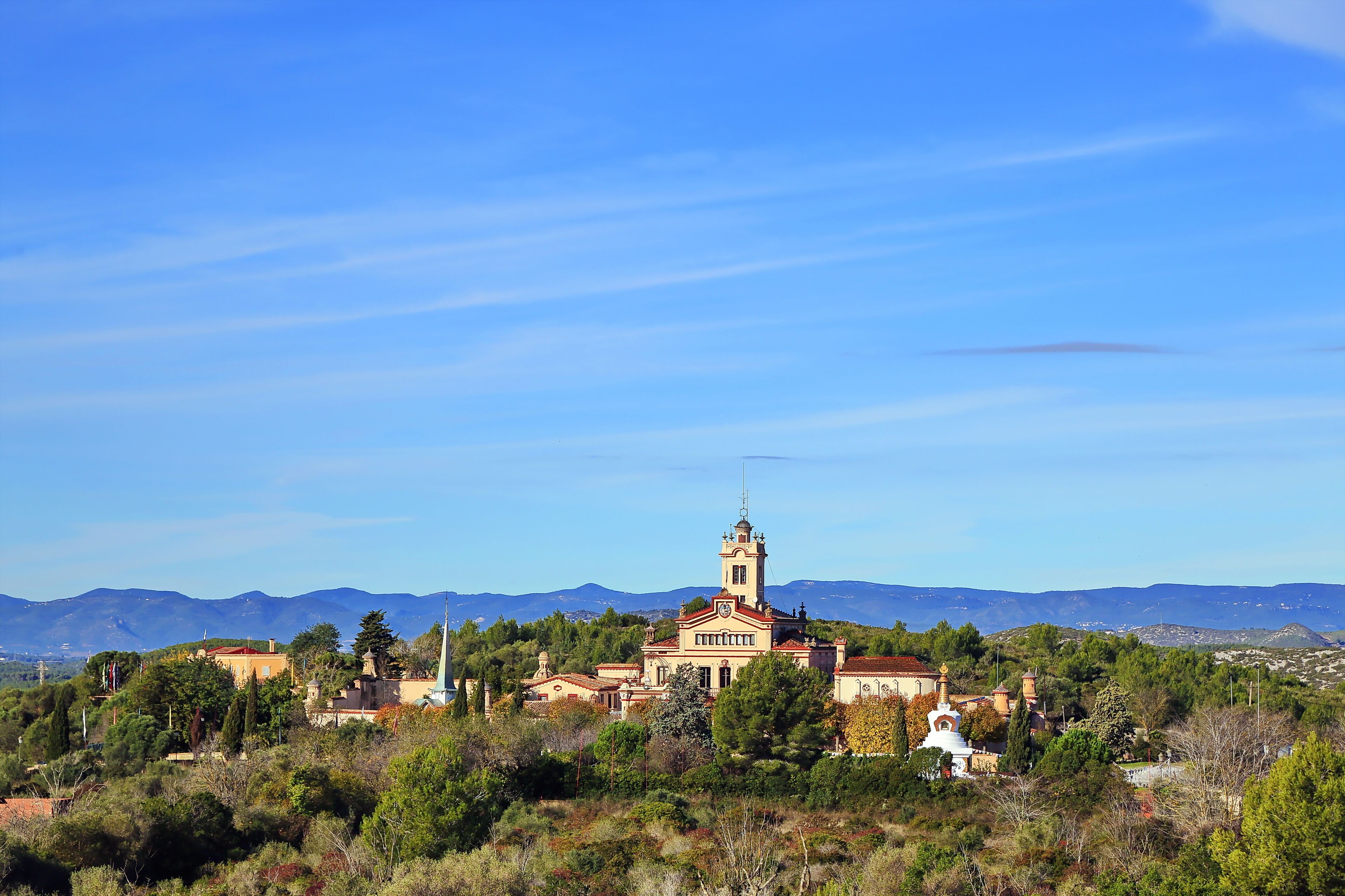 A historic building with a bell tower, surrounded by lush greenery and mountains in the background.